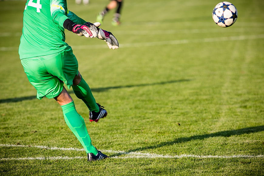 Soccer Goalkeeper Kicking Ball on Green Pitch