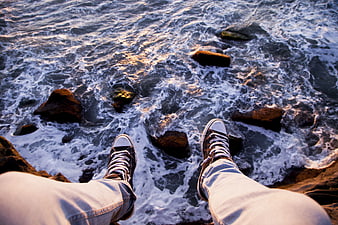 First-person view of legs dangling over ocean waves at sunset