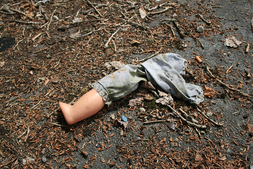 Broken doll leg lying on forest floor with twigs