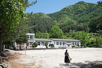 Woman Walking In Abandoned School Playground Surrounded By Lush Green Mountains