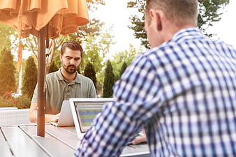 Two men working on laptops at outdoor cafe table