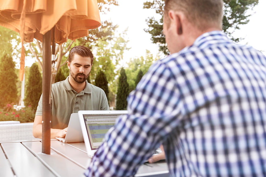 Two men working on laptops at outdoor cafe table