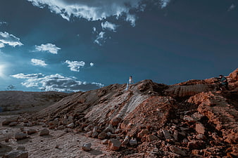 Woman in white dress standing on rocky hill under dramatic sky