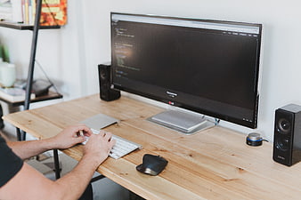 Man typing code on computer at wooden desk