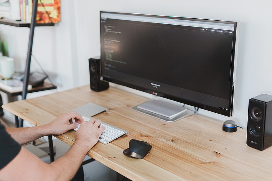 Man typing code on computer at wooden desk