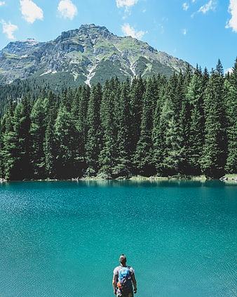 Hiker with backpack overlooking turquoise alpine lake and mountain