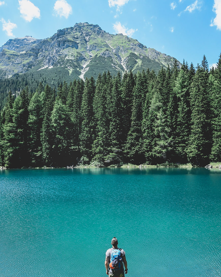 Hiker with backpack overlooking turquoise alpine lake and mountain