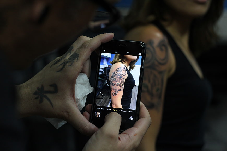 Tattoo artist photographing fresh sleeve tattoo on smartphone