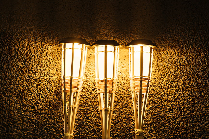 Three glowing bamboo-style lanterns against a textured wall
