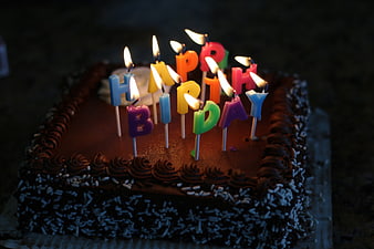 Chocolate birthday cake with lit letter candles spelling happy birthday