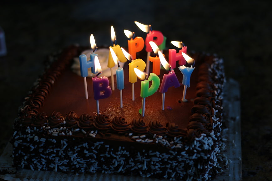 Chocolate birthday cake with lit letter candles spelling happy birthday