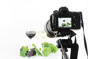 Professional DSLR camera on tripod photographing wine and grapes in studio