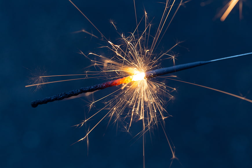 Close-up of burning sparkler with golden sparks against dark blue background