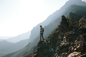 Hiker standing on rocky mountain ridge overlooking misty peaks