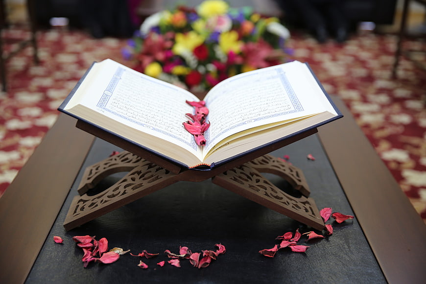 Open Quran on wooden stand with rose petals and floral background