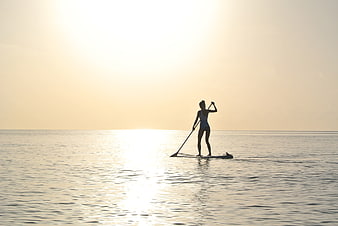 Woman Silhouette Paddleboarding on Calm Ocean at Sunset