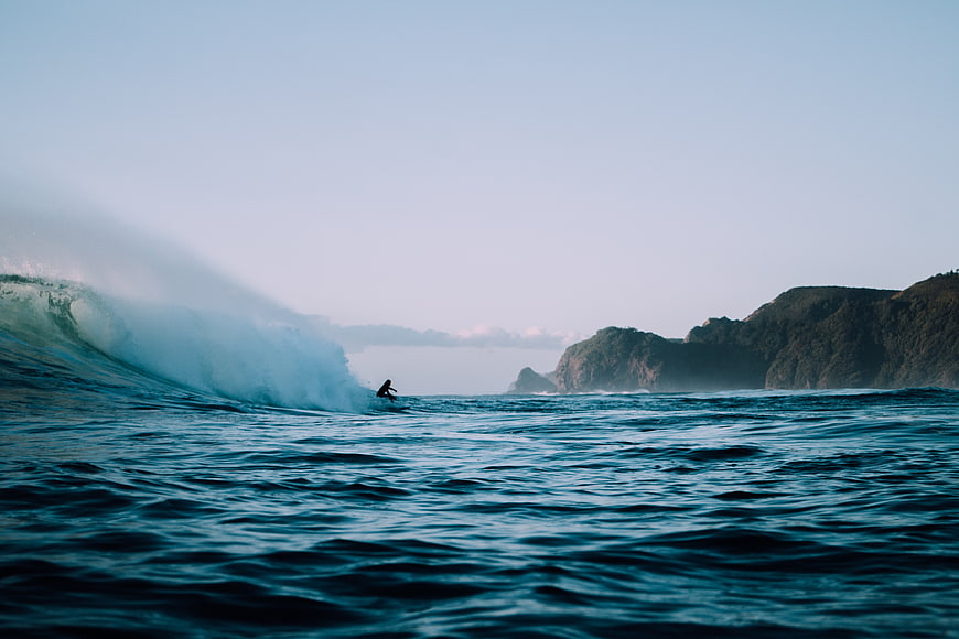 Surfer riding a large wave near coastal cliffs