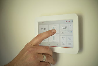 Hand adjusting digital thermostat on wall