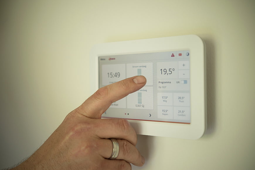 Hand adjusting digital thermostat on wall