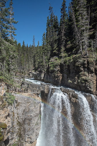 Majestic waterfall cascading down rocky cliffs with rainbow mist