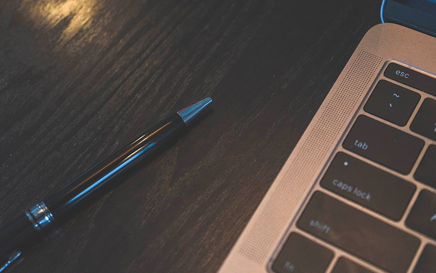 Close-up of black pen and laptop keyboard on dark wood desk