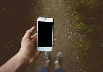 First-person view of hand holding smartphone on forest trail