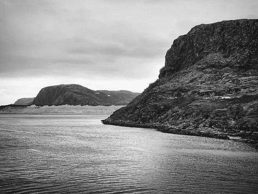 Black and white coastal landscape with rocky cliffs and calm water