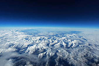 Aerial view of snow-covered mountain range above clouds