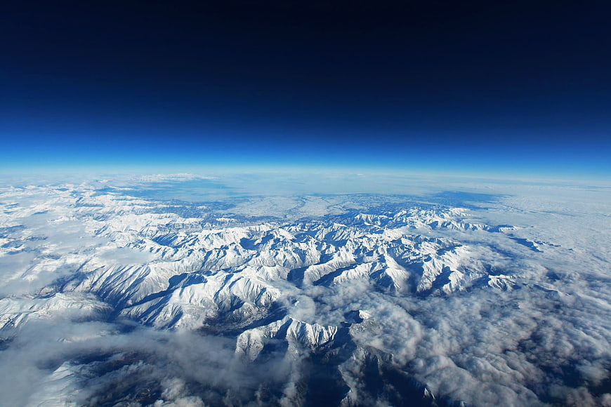 Aerial view of snow-covered mountain range above clouds