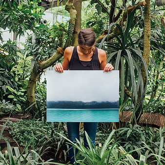 Woman holding landscape print in lush tropical greenhouse