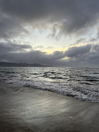Dramatic cloudy seascape with waves on sandy beach at dusk