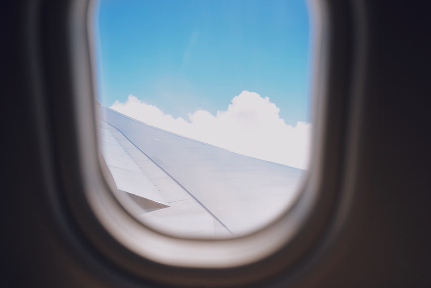 Airplane Wing View Through Window with Blue Sky and Clouds