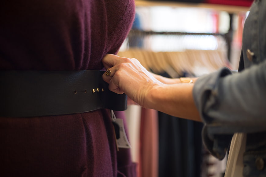 Woman adjusting belt on purple dress in clothing store
