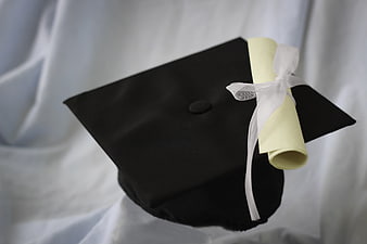 Black graduation cap with diploma scroll on white background