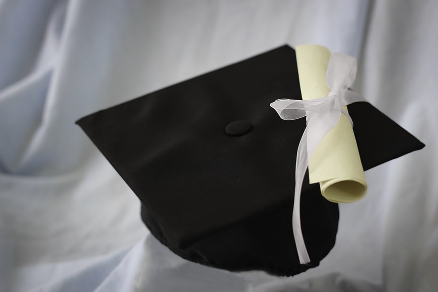 Black graduation cap with diploma scroll on white background
