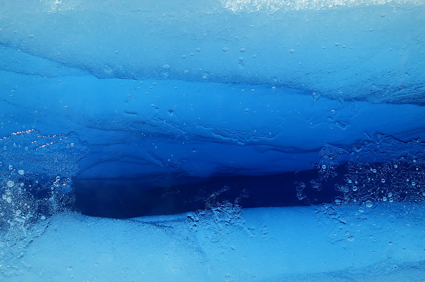 Underwater view of blue ice cave with air bubbles