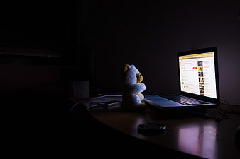 Teddy bear watching laptop screen in dark room