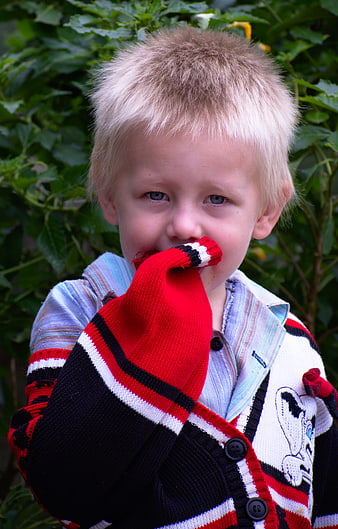 Cute blonde boy biting red sweater sleeve outdoors
