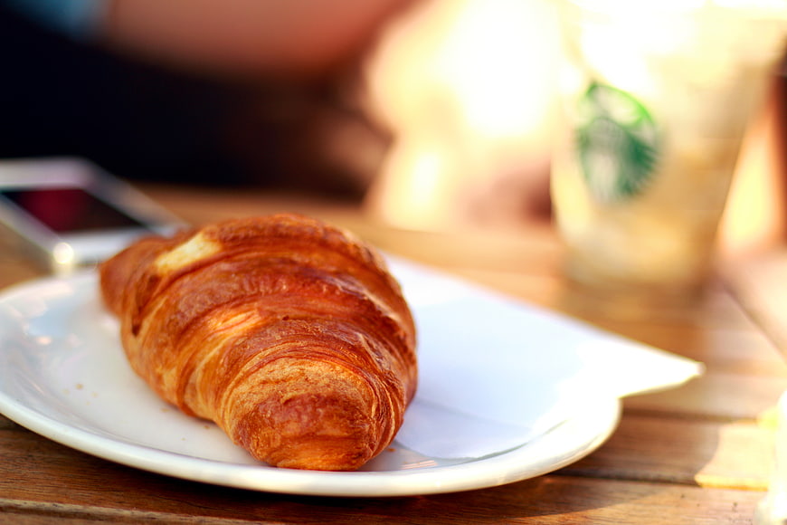 Golden Croissant on White Plate with Blurred Coffee Background