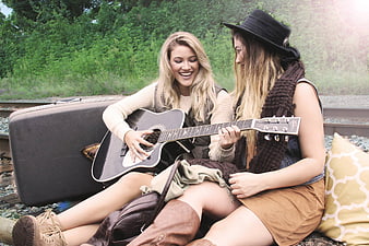 Two young women playing guitar on railroad tracks
