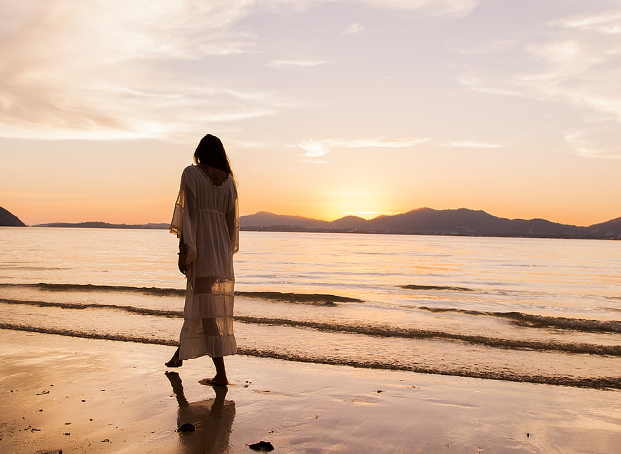 Woman in White Dress Walking on Beach at Sunset