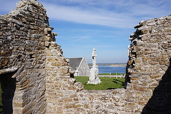 Ancient stone ruins framing a Celtic cross and coastal view