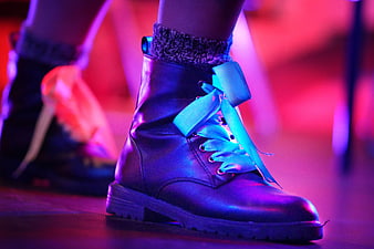 Close-up of black combat boots with blue ribbon laces under neon light
