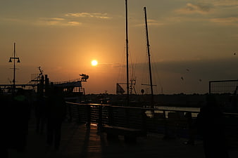 Silhouetted Harbor Sunset with Sailboats and Walking Figures