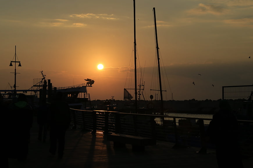 Silhouetted Harbor Sunset with Sailboats and Walking Figures