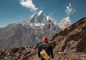 Hiker with yellow bag walking on mountain trail towards snowy peaks