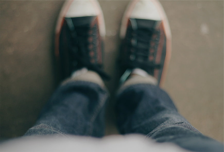 First-person view of sneakers and jeans on pavement