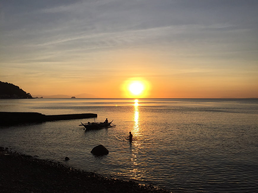 Silhouette of Fisherman and Boat at Golden Sunset Over Calm Sea