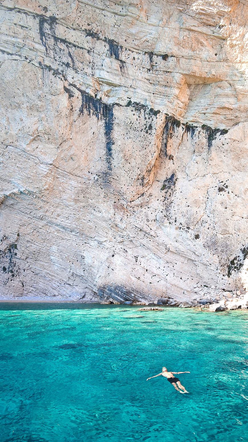 Man swimming in turquoise water near white cliffs