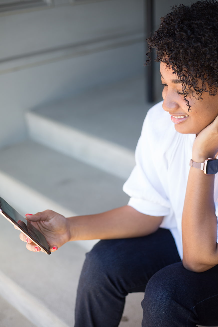 Smiling woman with curly hair using smartphone on stairs